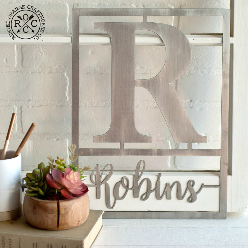 Metal sign with family name and monogram leaning on shelf.