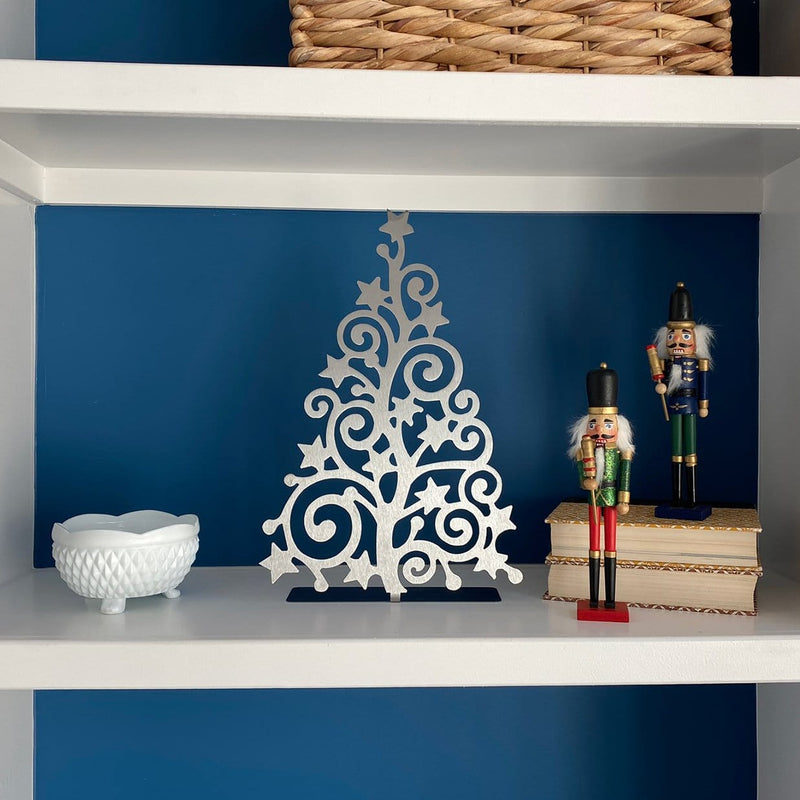 Metal Christmas tree cutout with swirls and stars throughout, standing on shelf next to Christmas nutcrackers.