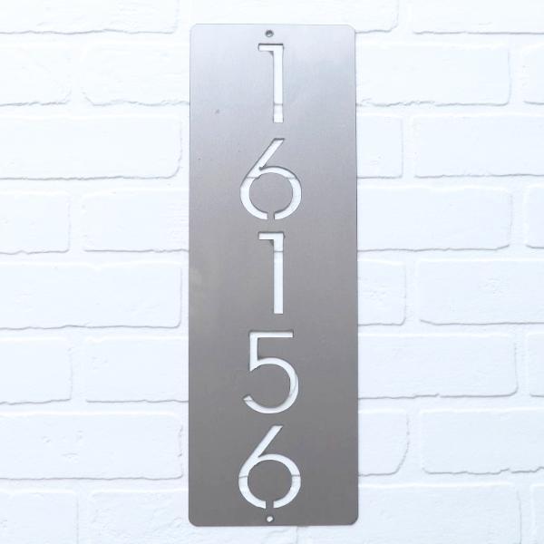 Metal vertical house number hanging on white brick.