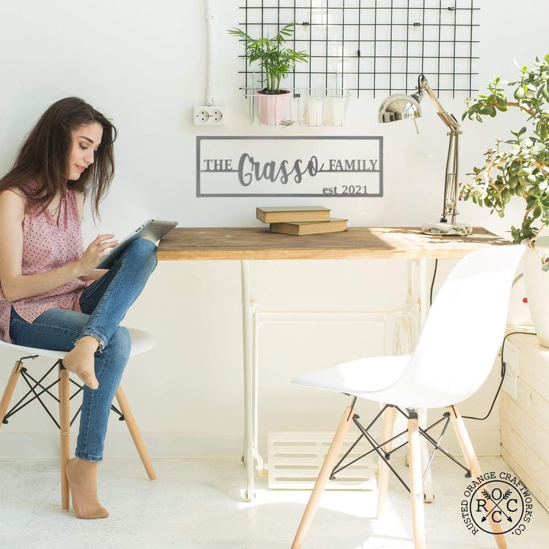 Personalized metal family name and established sign hanging above table, girl sitting at table on computer.