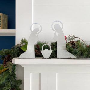 3 piece metal nativity scene silhouette standing on mantel in front of green garland.