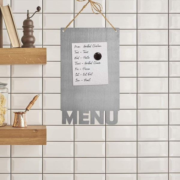 Rectangle magnetic board with menu etched at the bottom with handwritten weekly menu held by magnets, hanging on wall by shelves in kitchen.