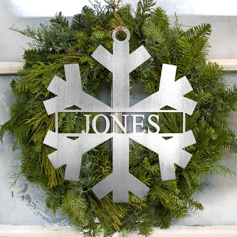 Metal snowflake with last name in center within pine wreath.