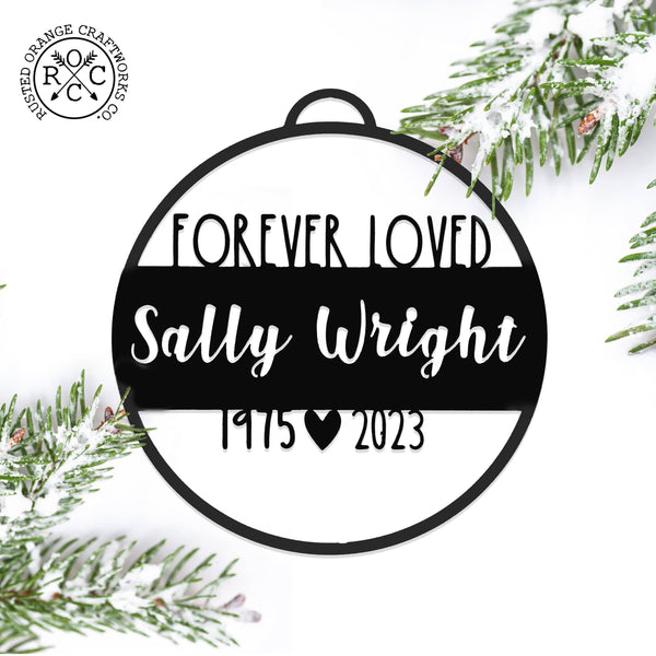 memorial ornament laying flat next to pine needles covered in snow