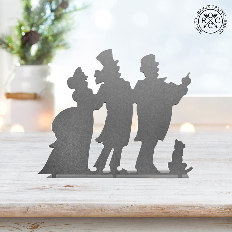 Metal silhouette of 3 Christmas carolers standing on a table.