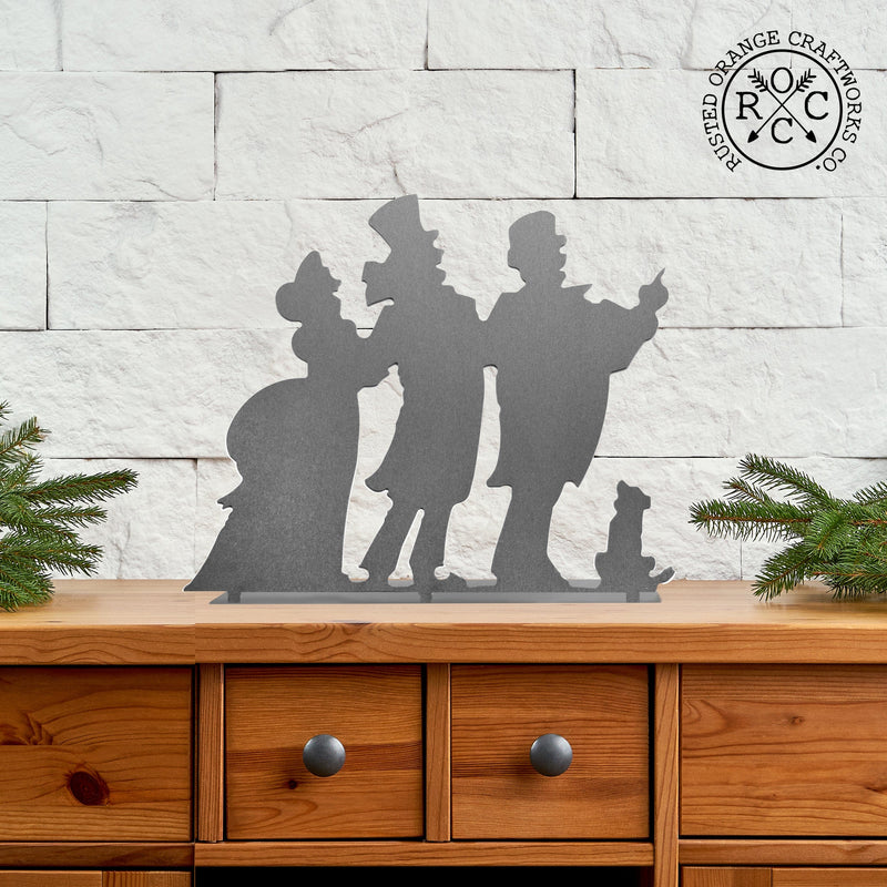 Metal silhouette of 3 Christmas carolers standing on a table.