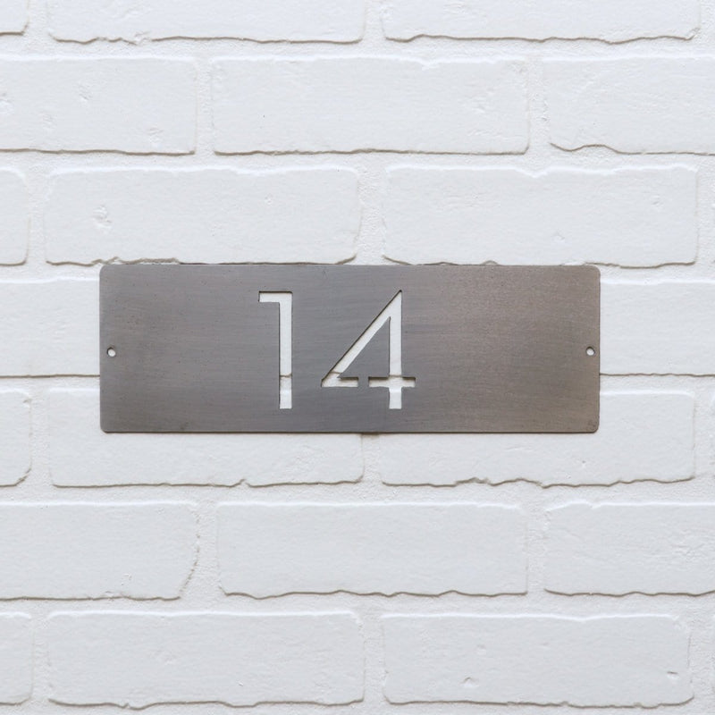 Metal horizontal house number hanging on white brick.