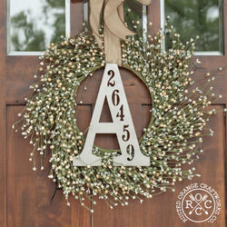 Metal letter with house number inscribed, hanging with wreath on front door.