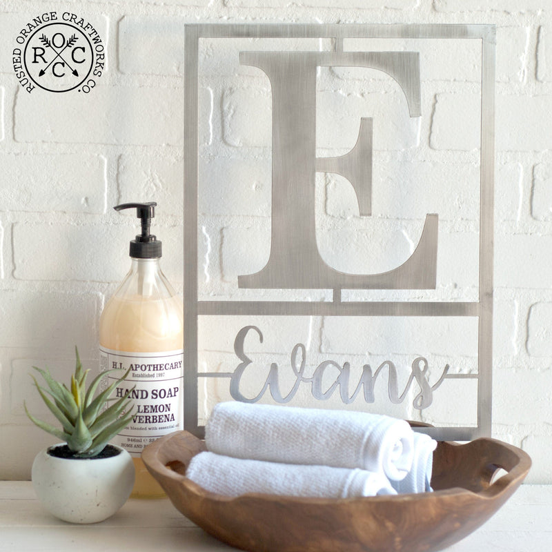 Metal sign with family name and monogram leaning against wall on bathroom counter.