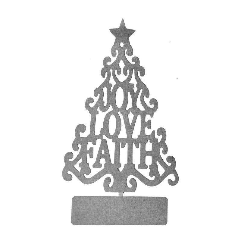 Metal Christmas tree cutout with words joy love faith in the center, standing on shelf next to plant and photo.