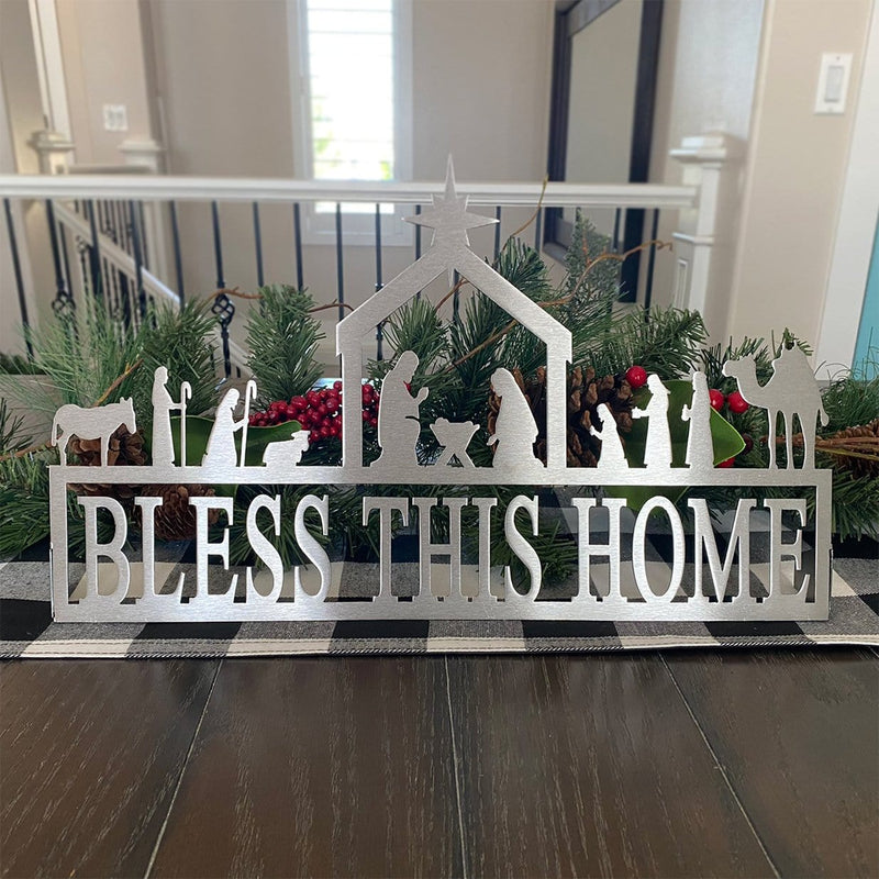 Metal sign saying bless this home below nativity scene silhouette, sitting on table.
