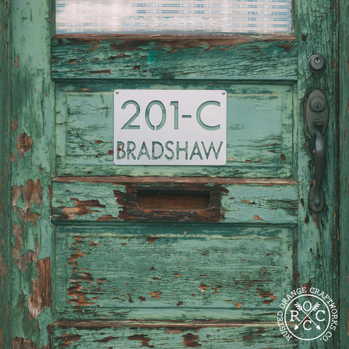 Metal rectangle sign with unit number and last name, hanging on door.