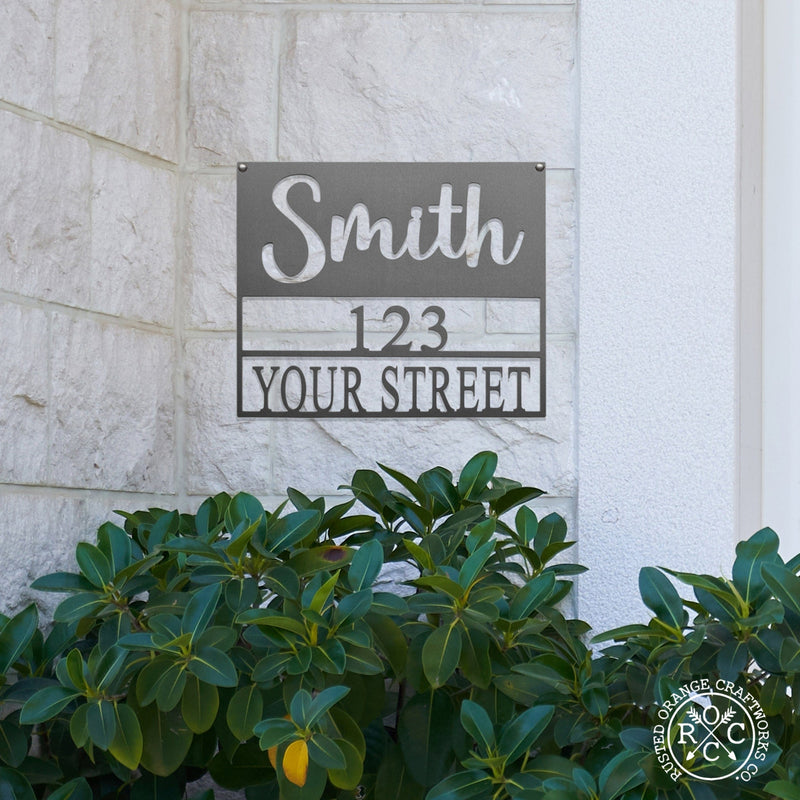 Square metal sign with last name and address hanging outside on house.