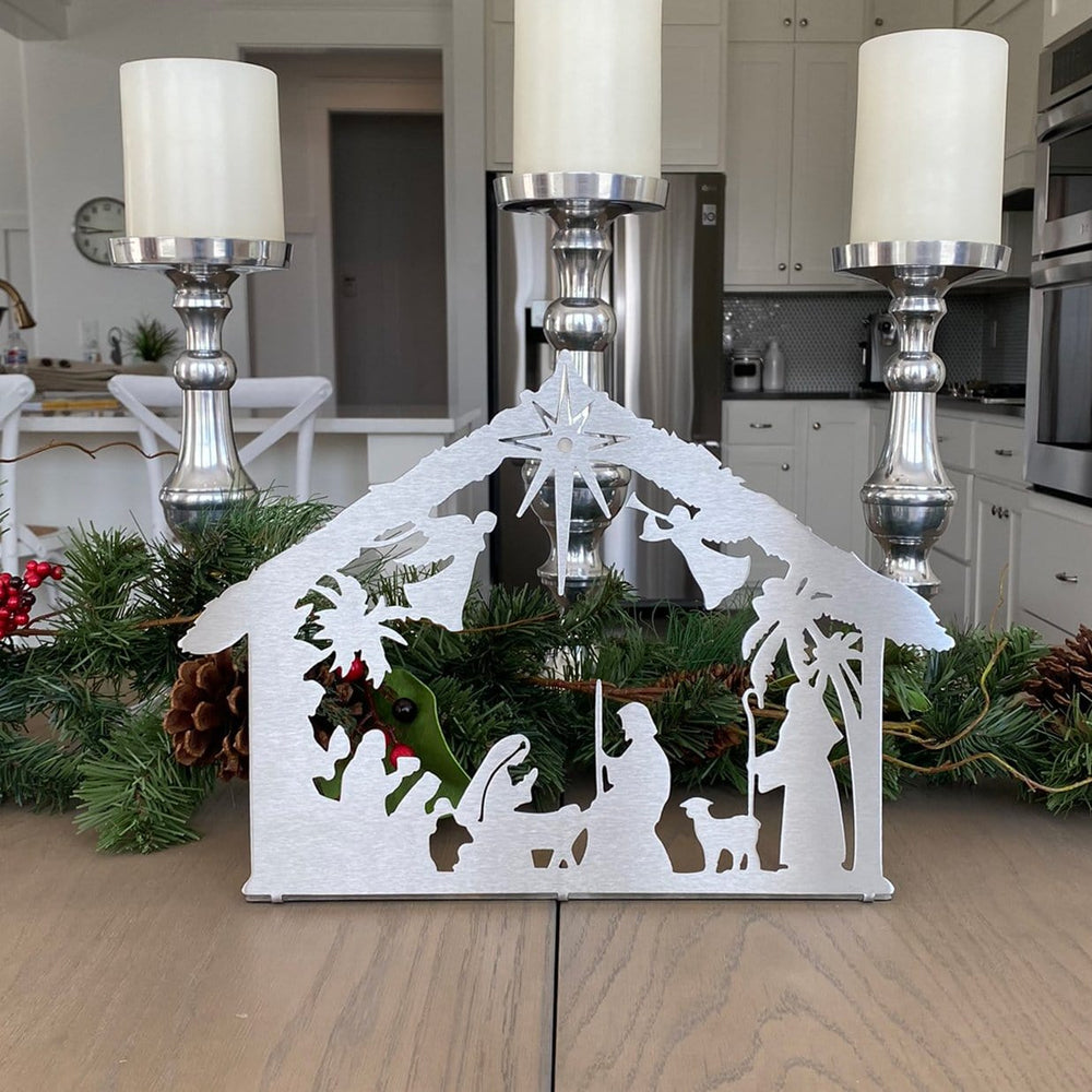 Metal nativity scene silhouette standing on table with candles and garland.
