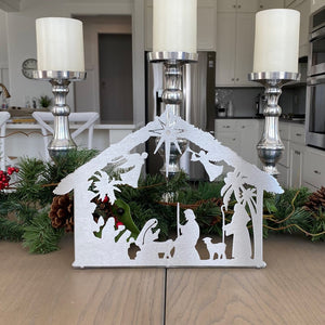 Metal nativity scene silhouette standing on table with candles and garland.