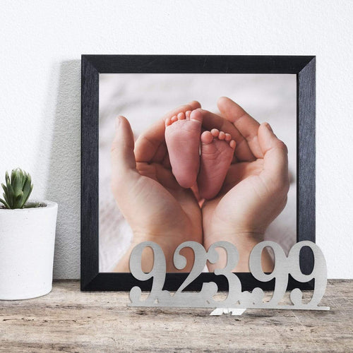Metal sign with date 9/23/99 standing on shelf next to photo of baby feet.