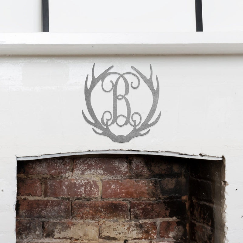 Metal deer antlers with monogram B in the middle, hanging on wall above fireplace.