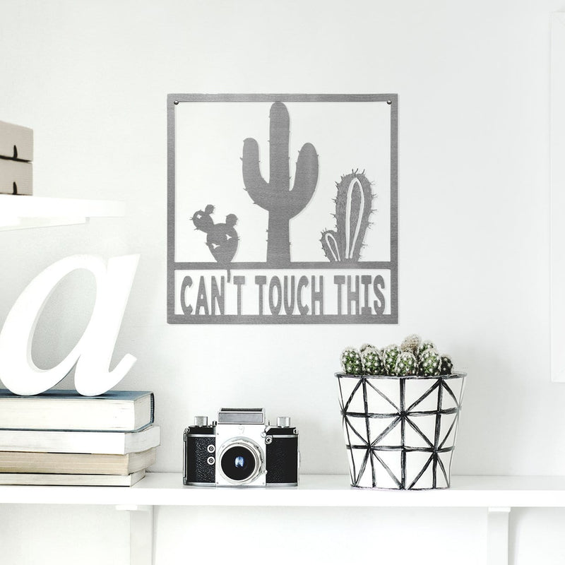 Square metal sign with cactus that says can't touch this, hanging on wall.