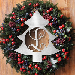 Metal Christmas tree shape cutout with monogram in the center, hanging within Christmas wreath on wall.