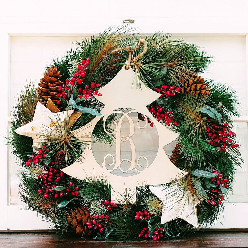 Metal Christmas tree shape cutout with monogram in the center, sitting within Christmas wreath on shelf.