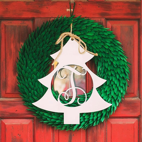 Metal Christmas tree shape cutout with monogram in the center, hanging within Christmas wreath on door.