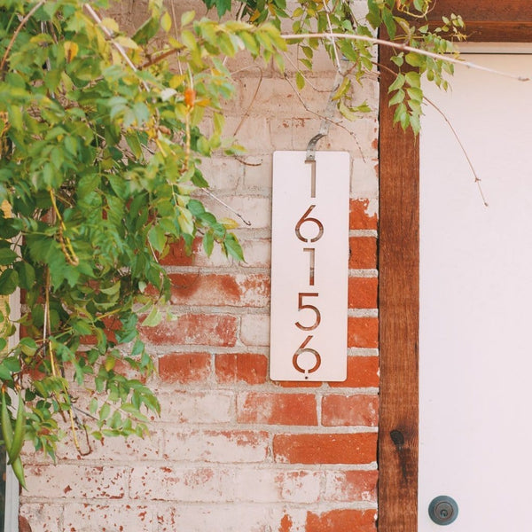 Metal vertical house number hanging outside brick house next to door.