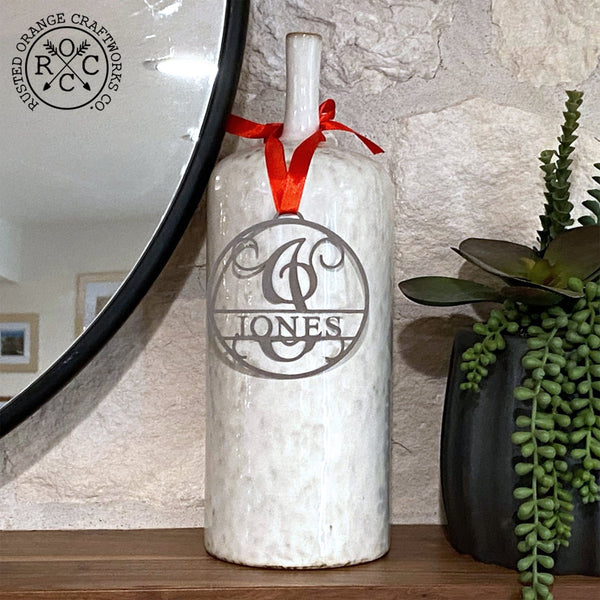 Circle metal ornament with name and monogram hanging on mantel with other decor.