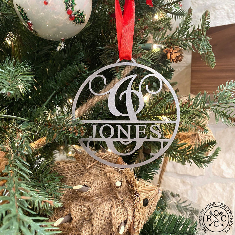 Circle metal ornament with name and monogram hanging on Christmas tree.