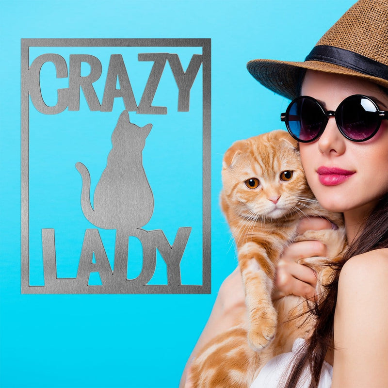 Rectange metal sign that says crazy lady with a cat etched in the center, hanging next to woman in hat and sunglasses holding cat.
