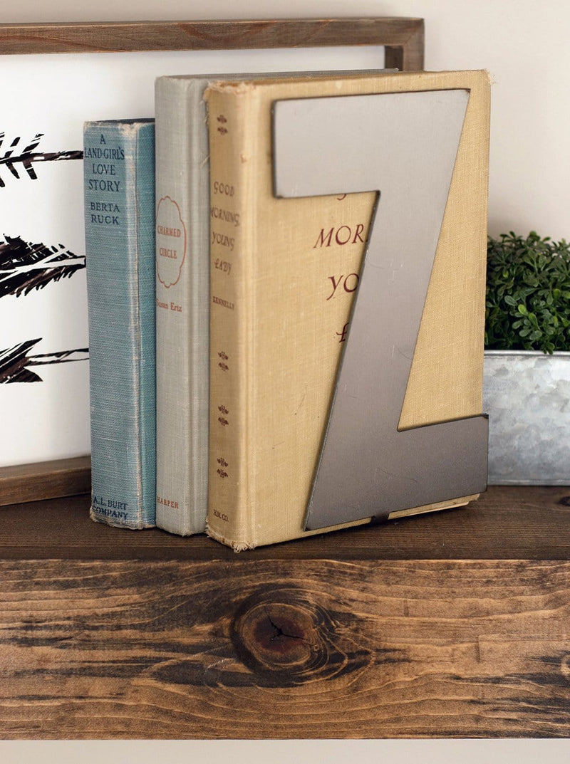 Metal letter Z with bent tab on bottom standing on shelf with books.