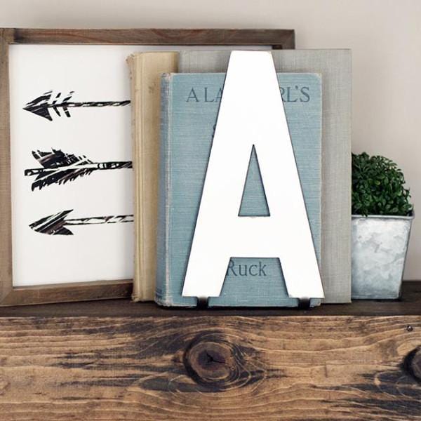 Metal letter A with bent tab at bottom standing on shelf with books.