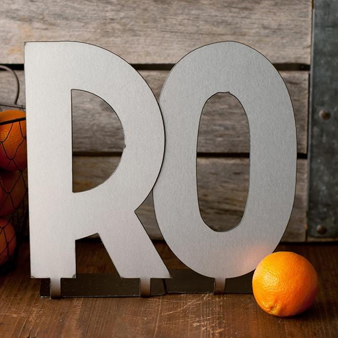 Metal letters R and O with bent tabs on bottom, standing next to basket of oranges.