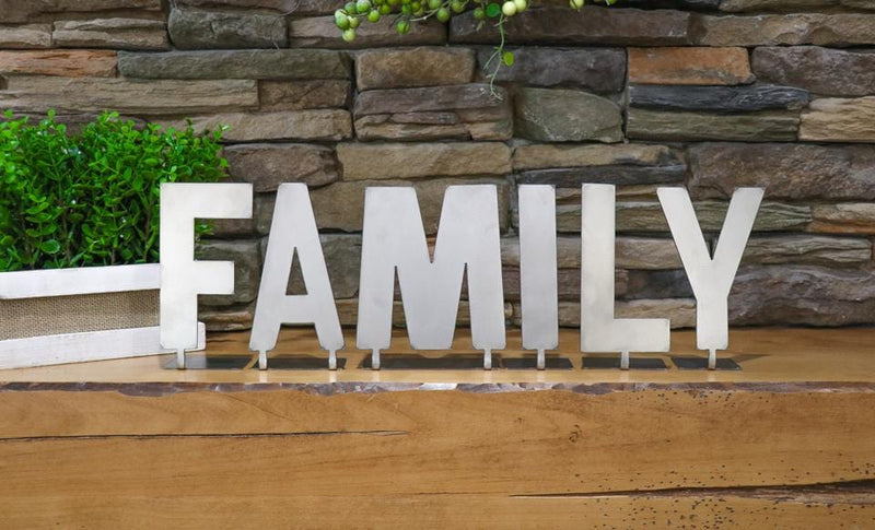 Metal letters with bent tabs on bottom spelling out the word family, standing on mantel next to plant.