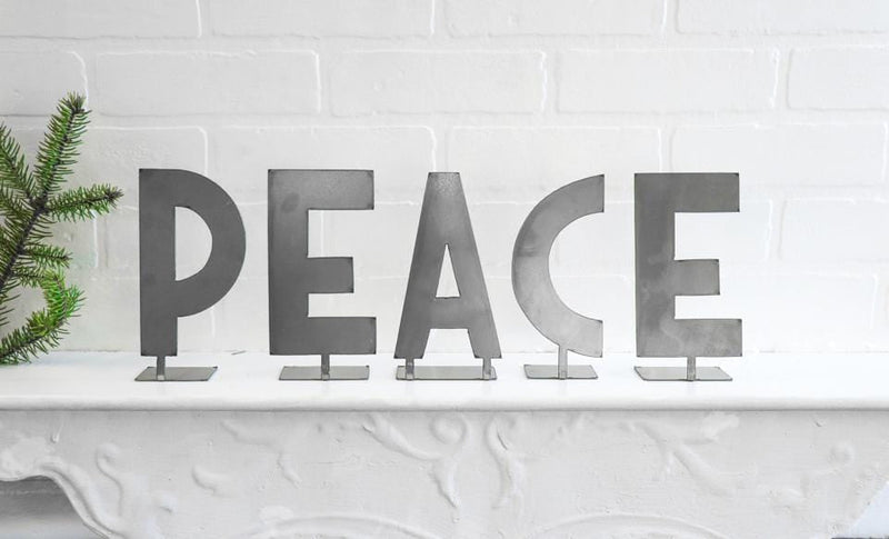 Metal letters with bent tabs on the bottom standing on mantel spelling out the word peace.