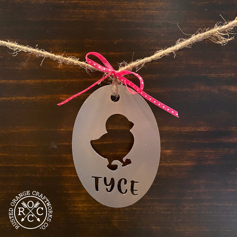 Wood background with oval shaped metal ornament with cutout of baby chick above custom name of Tyce.