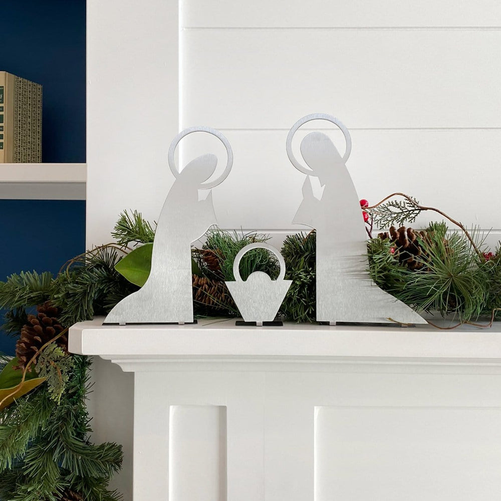 3 piece metal nativity scene silhouette standing on mantel in front of green garland.