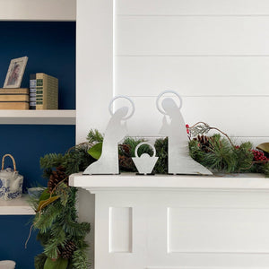 3 piece metal nativity scene silhouette standing on mantel in front of green garland.
