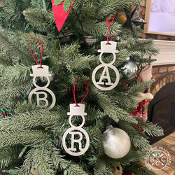 3 metal snowman shaped ornaments with monogram hanging from Christmas tree.