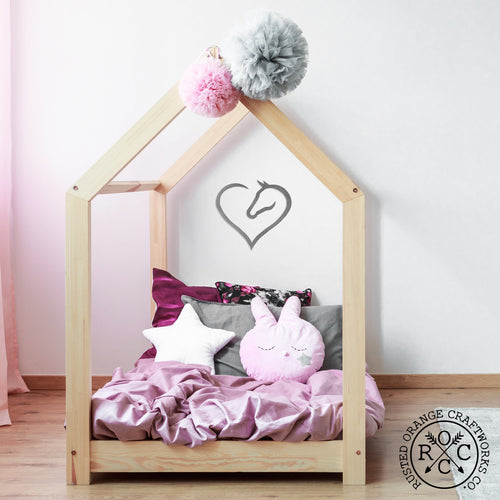 Metal heart shaped horse silhouette hanging on wall above child's bed.