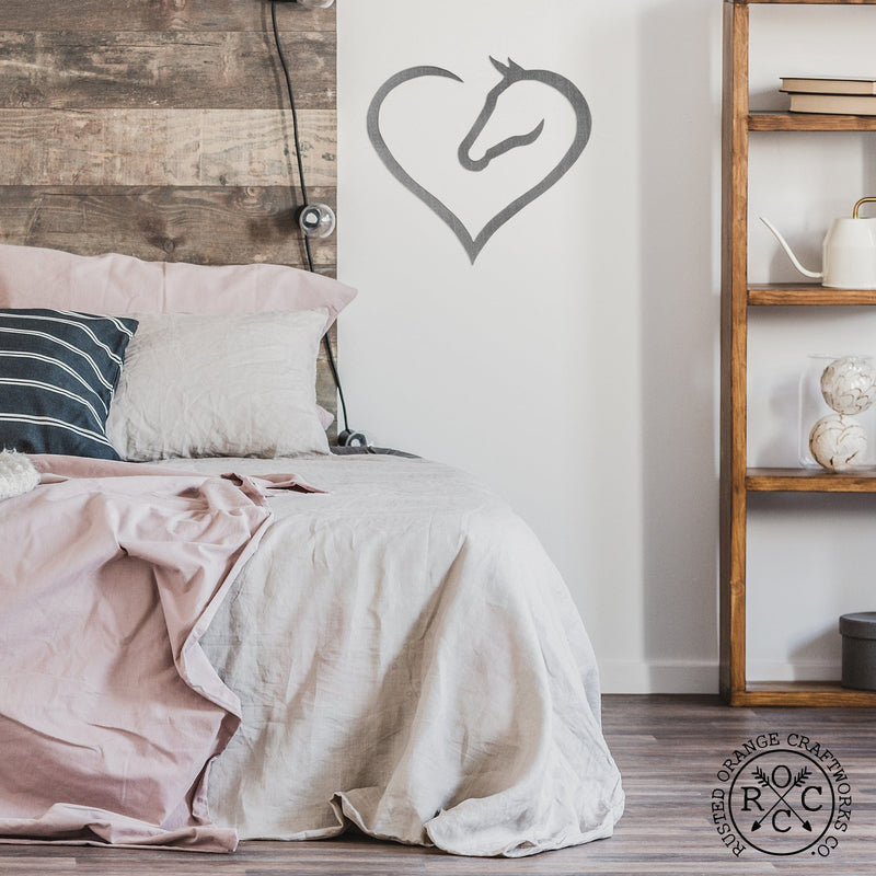 Metal heart shaped horse silhouette hanging on bedroom wall in between bed and shelves.