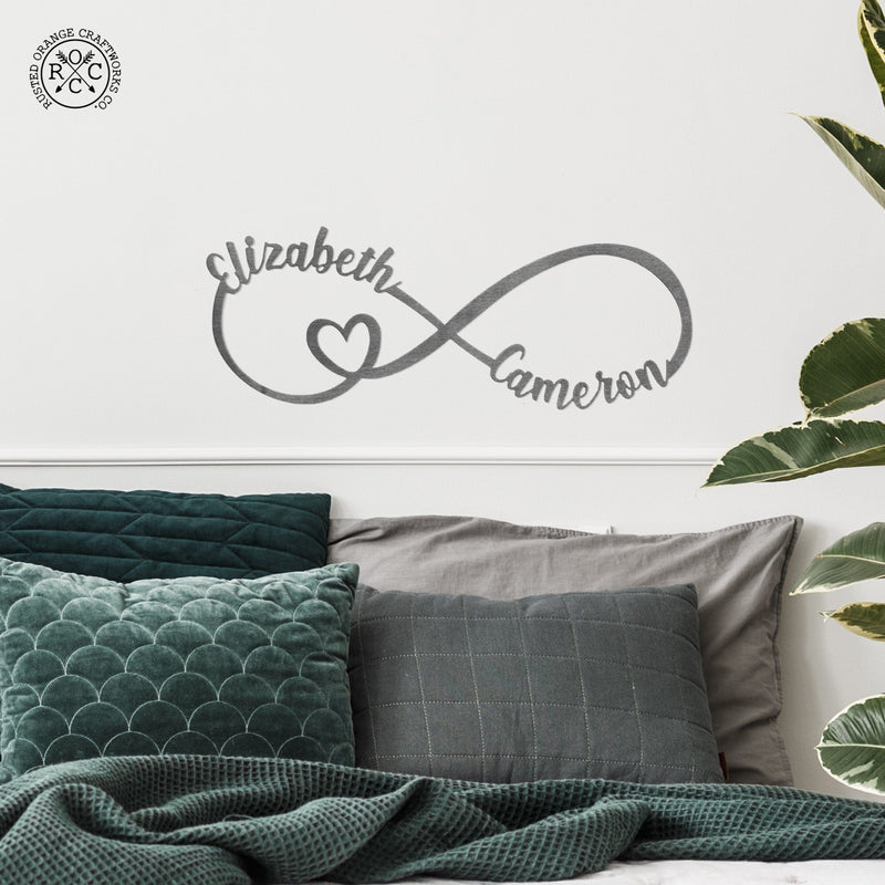 picture of metal infinity sign with Elizabeth and Cameron personalization and heart hanging over bed on a wall with a tall plant next to bed