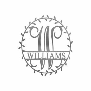 Metal circle sign with name and monogram in center and laurel leaves along edge, against white background.