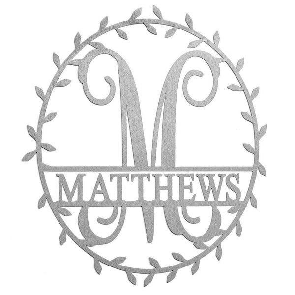 Metal circle sign with name and monogram in center and laurel leaves along edge, against white background.