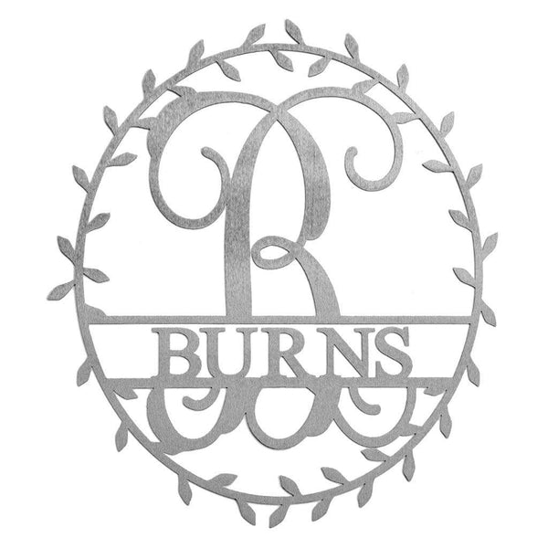 Metal circle sign with name and monogram in center and laurel leaves along edge, against white background.