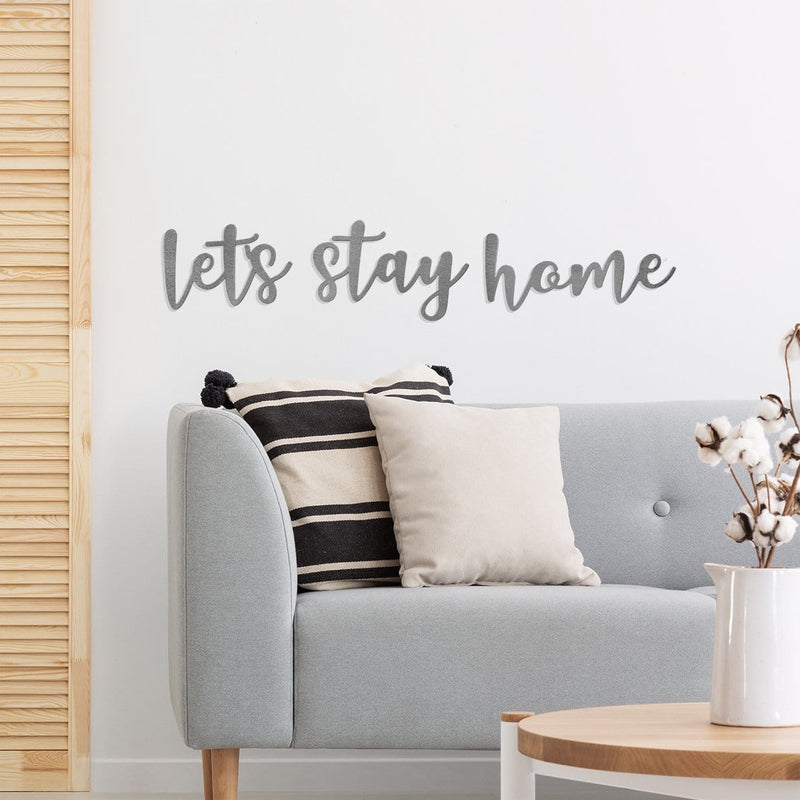 Metal sign saying let's stay home hanging on wall above couch.