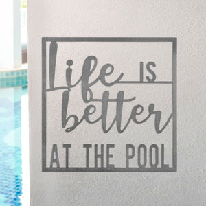 Square metal sign saying life is better at the pool, hanging on wall at swimming pool.