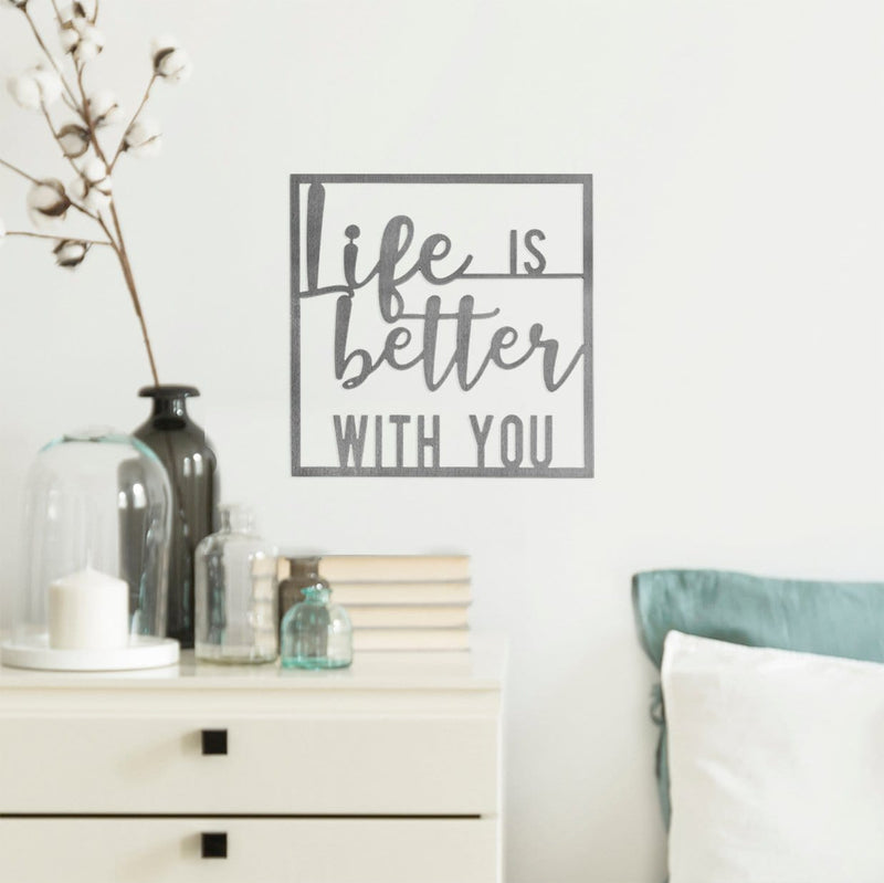 Square metal sign saying life is better with you, hanging on wall above bed.