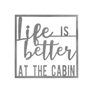 Square metal sign saying life is better at the cabin, shown against white background.