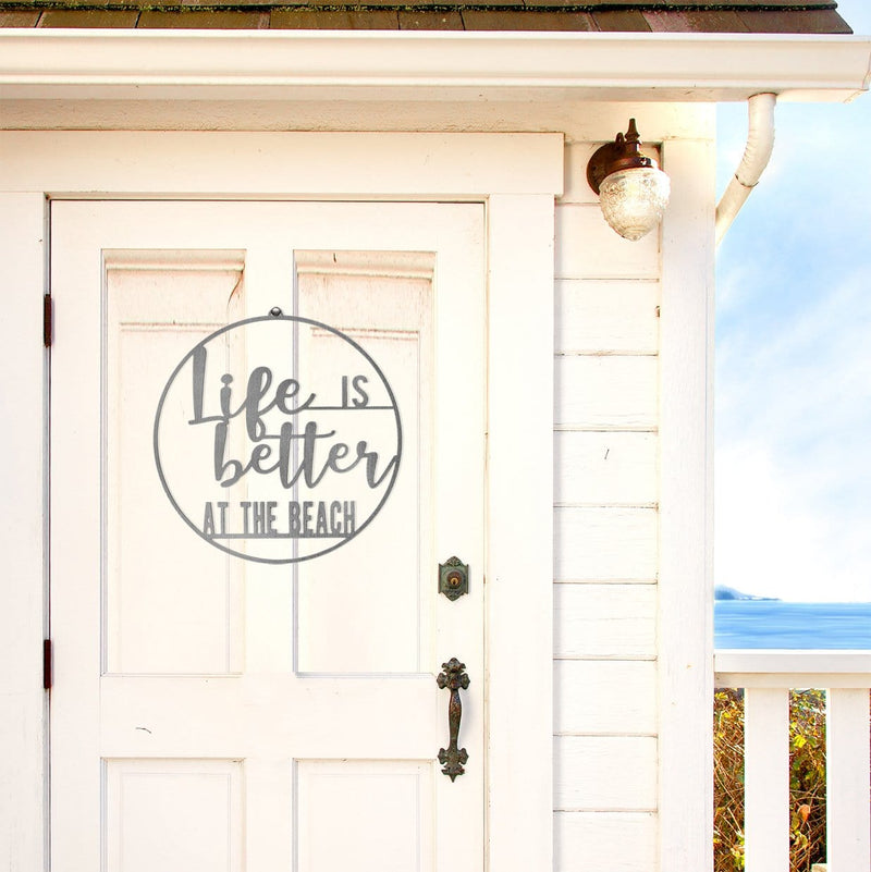 Round metal sign saying life is better at the beach, hanging on front door of beach house.