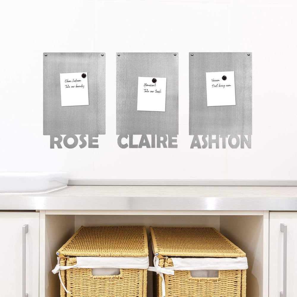 3 rectangle magnetic boards with names etched at the bottom with papers held by magnets on them, hanging on wall above shelf.